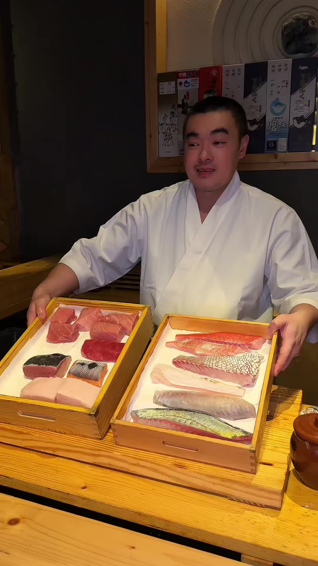 A Nishiyama chef presenting two wooden trays of seasonal fish